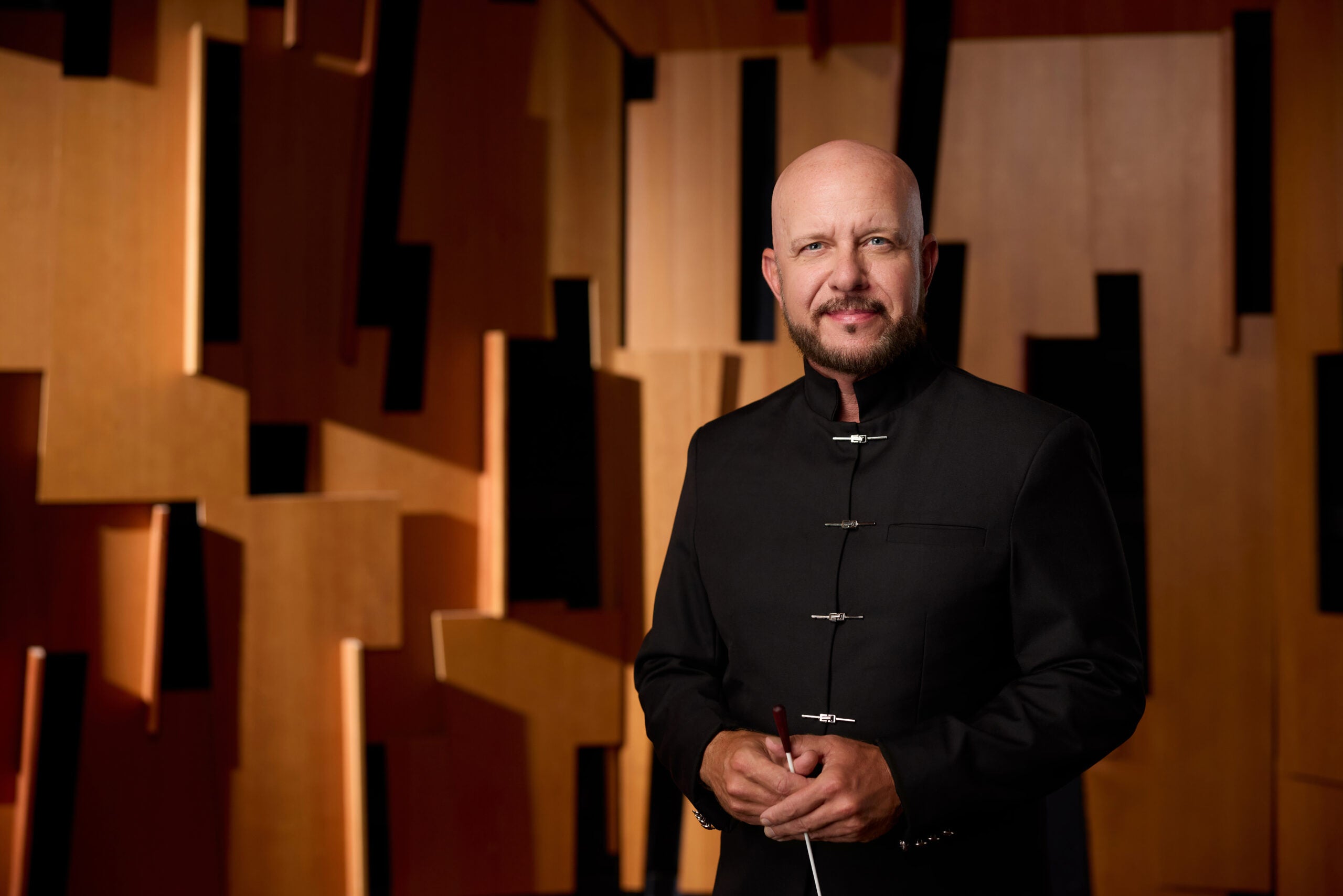 Man in black jacket standing against a backdrop of wood baffle in the recording studio.