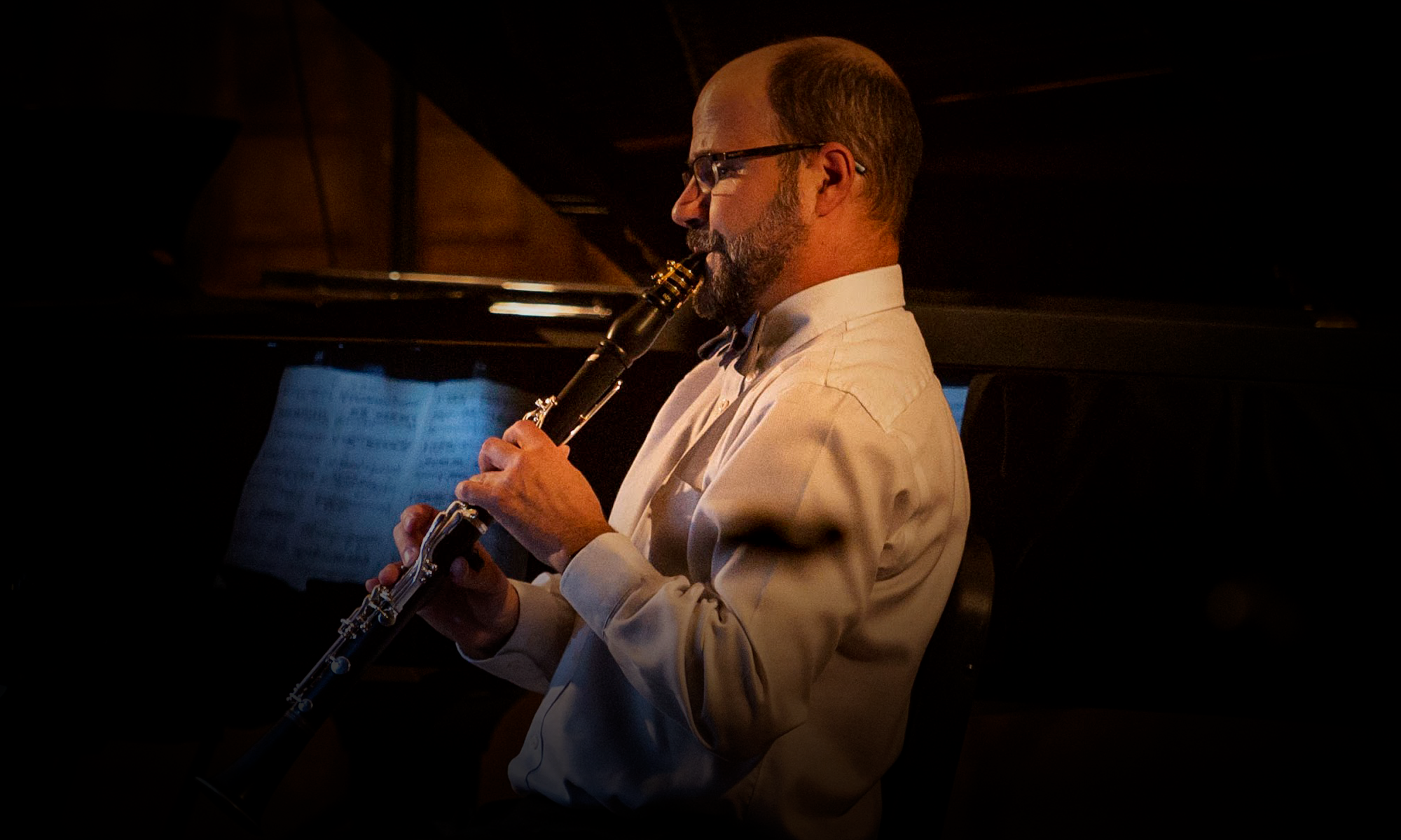 Man wearing a white suit standing in a profile pose, playing the clarinet