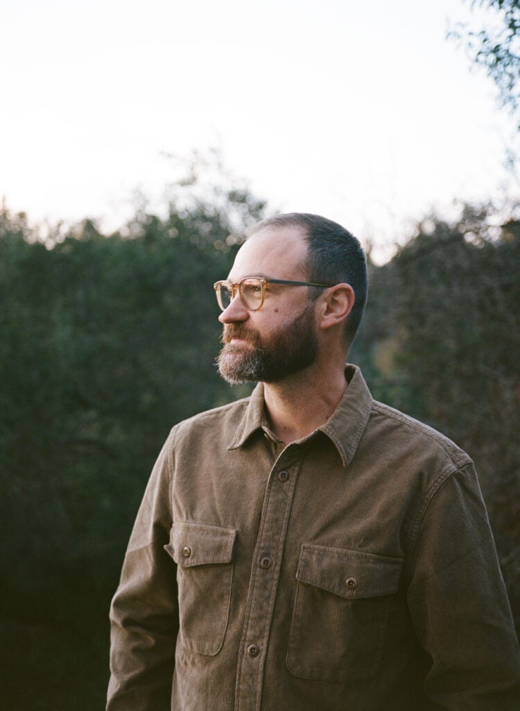 Profile of man with beard and glasses against a nature background.