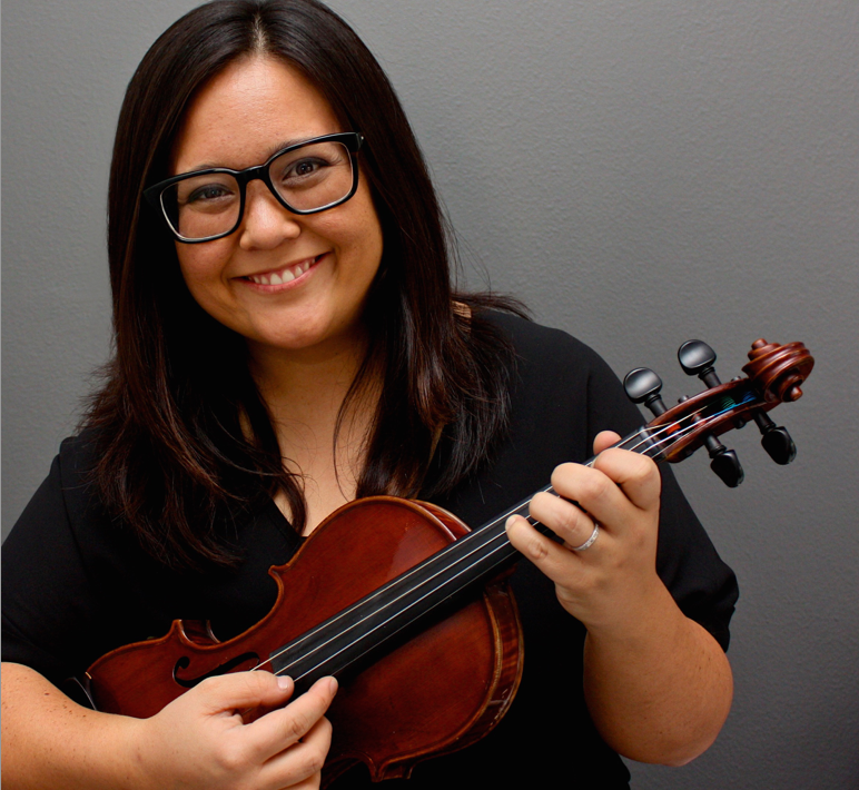 A woman, wearing black and holding a violin, in front of a gray background.