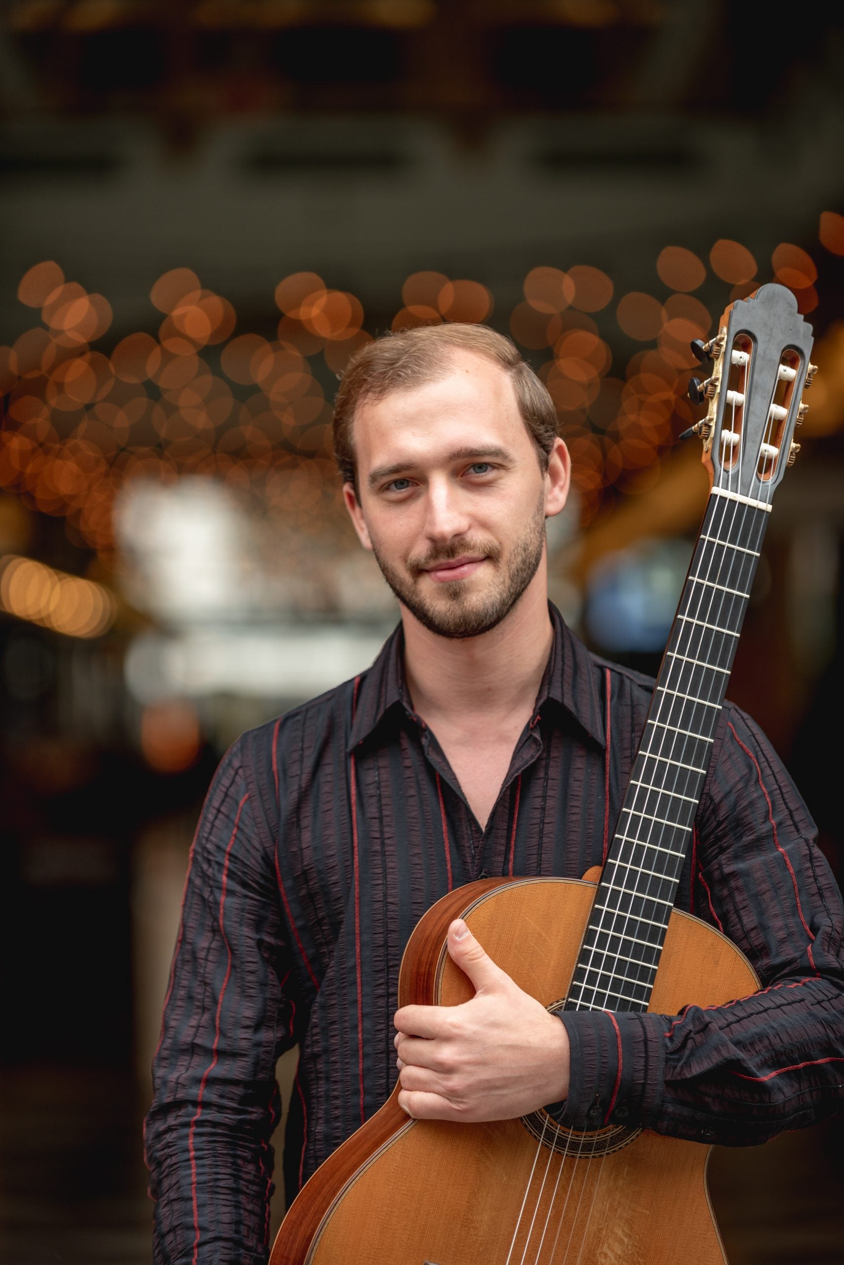Man wearing a dark striped button-up shirt while holding a guitar.