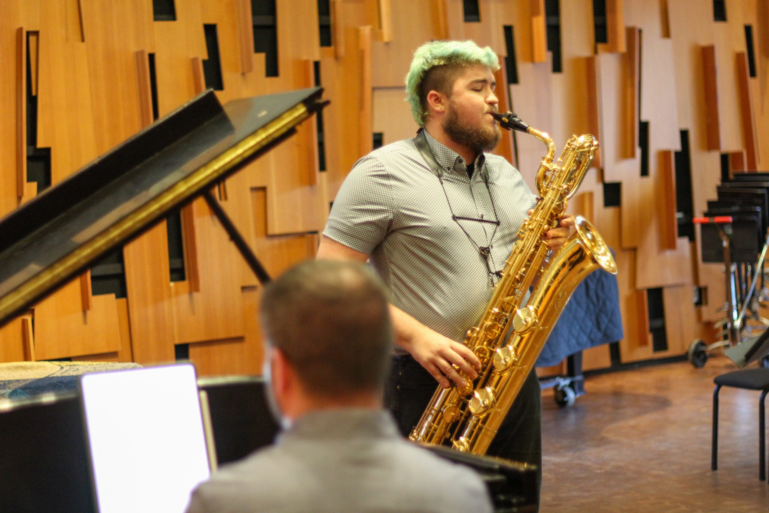 Man in checkered shirt playing a gold baritone saxophone.