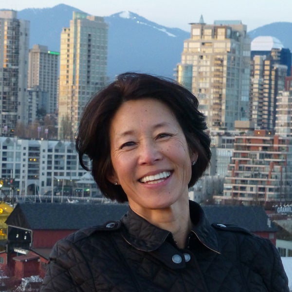 Woman with short dark hair wearing a collared dark jacket with a city skyline as background