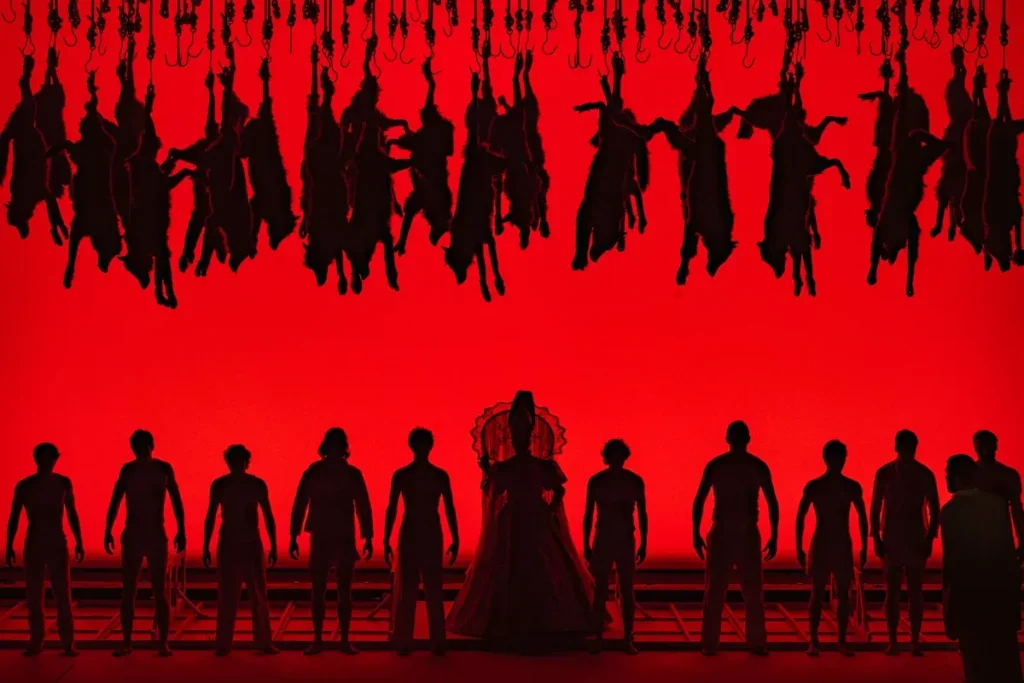 ON a red background, silhouettes of people standing beneath wolf pelts hung upside down from the ceiling.