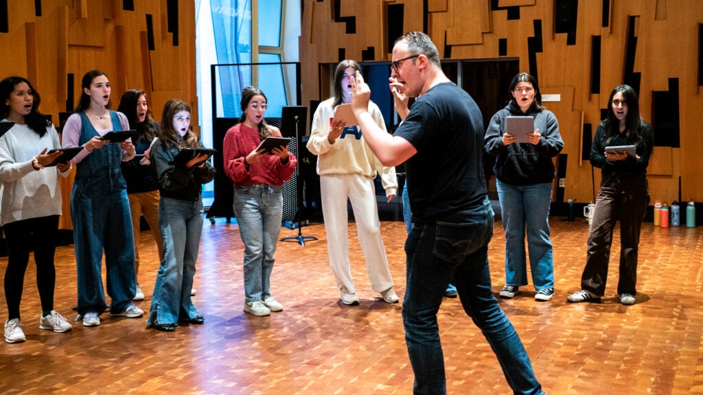 Man in black shirt directing a group of singers dressed casually.