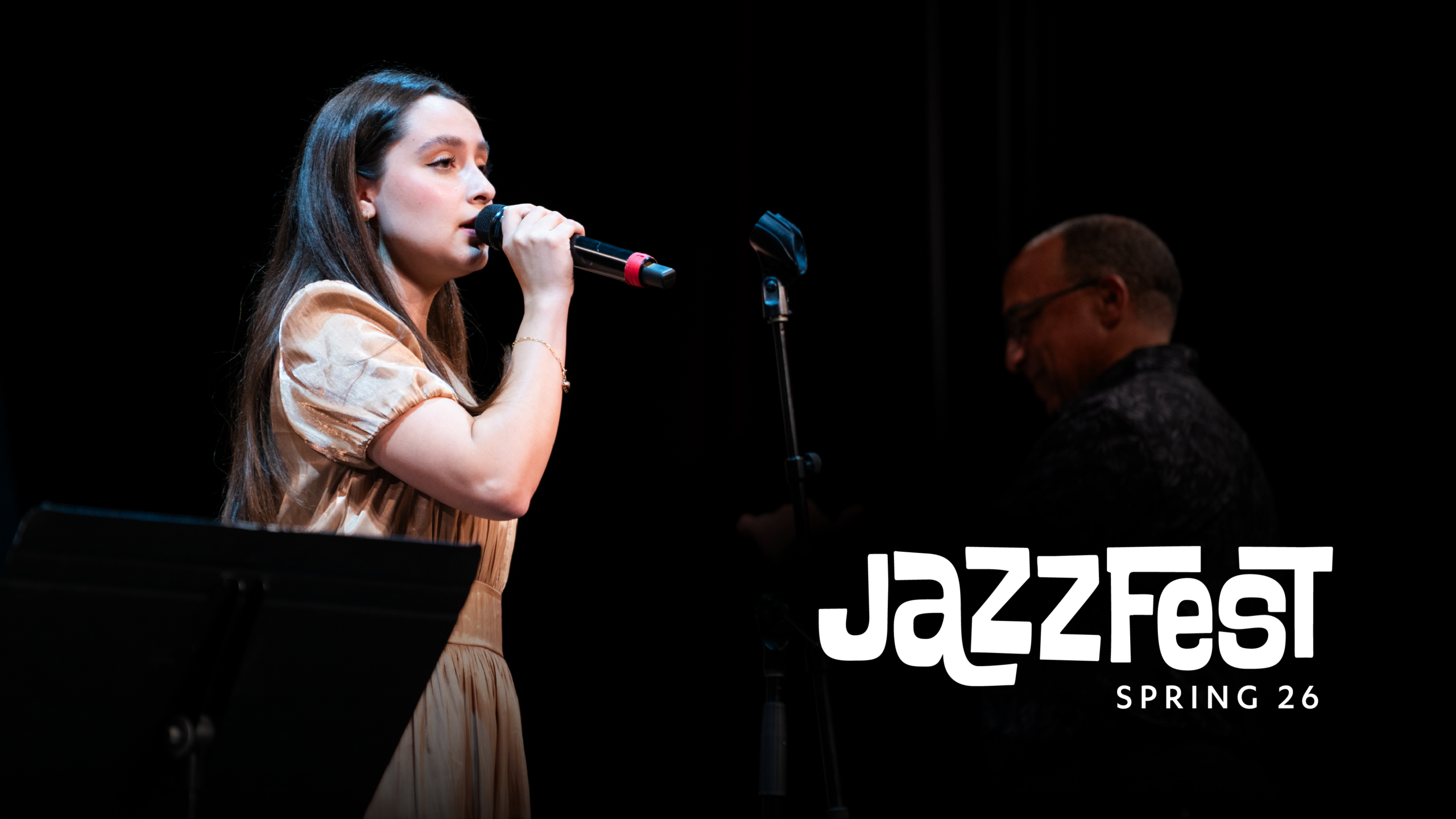 Woman with microphone against a black background and the words Jazzzfest Winter 26 in graphic text.
