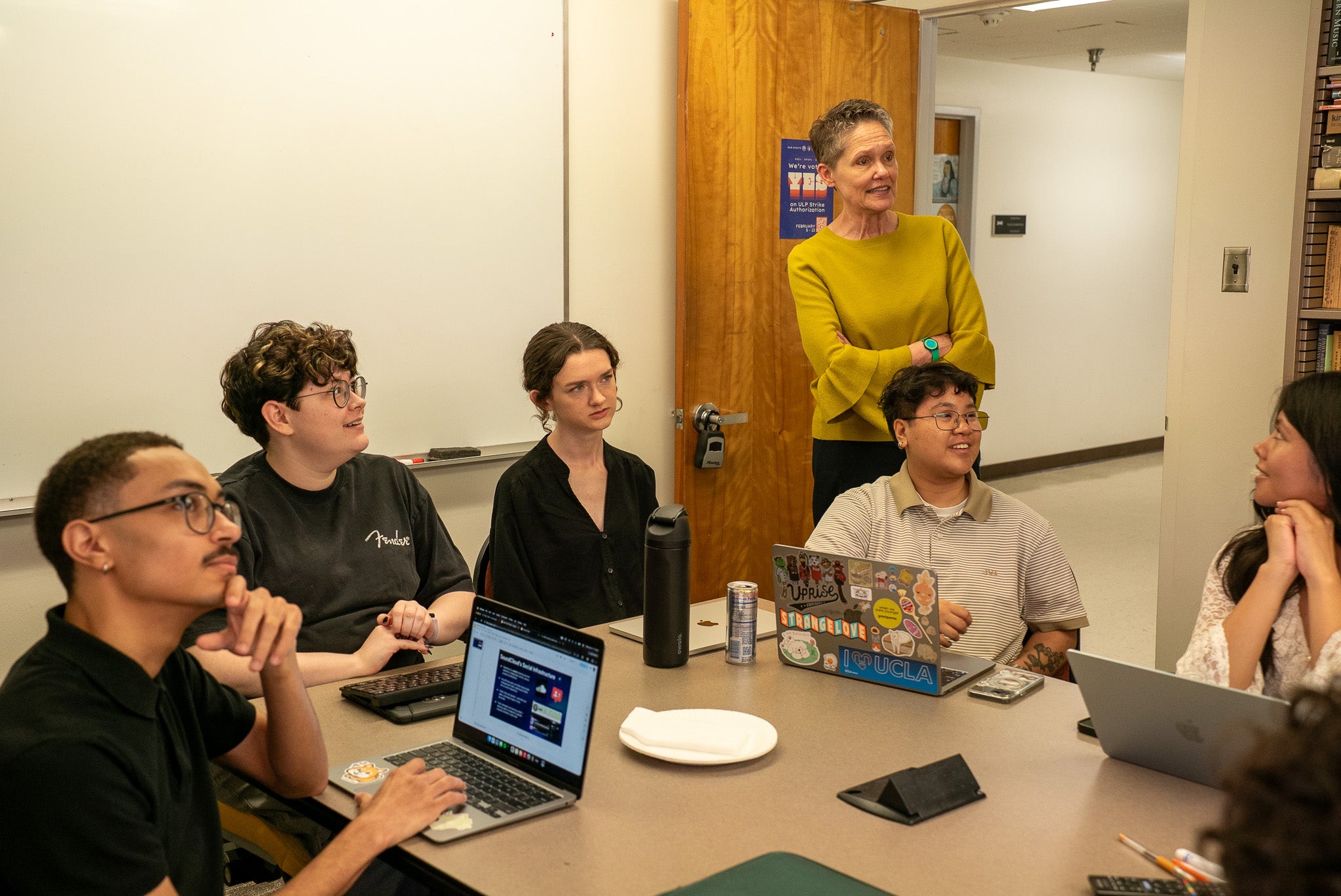 Seminar room with professor in a yellow shirt reviewing student work.
