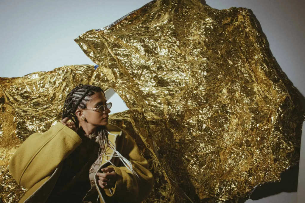 Woman in yellow standing in front of a golden sculpture.