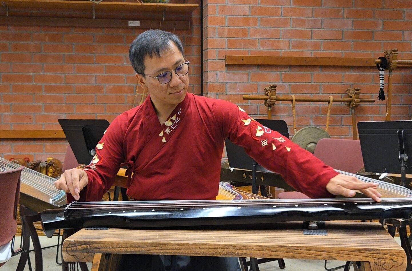 man in red tunic playing a stringed Chinese instrument.