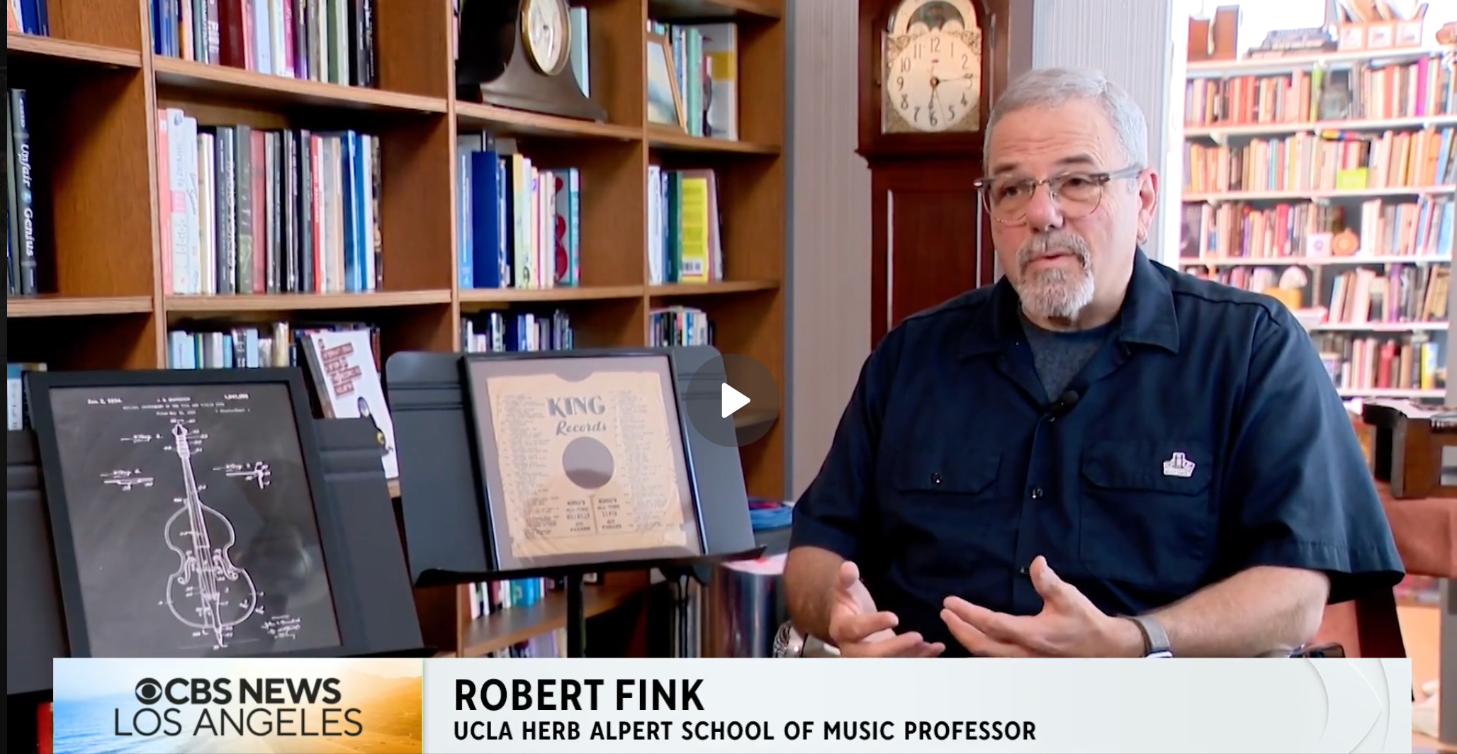 man sitting next to a bookshelf being interviewed by CBS Los Angeles.
