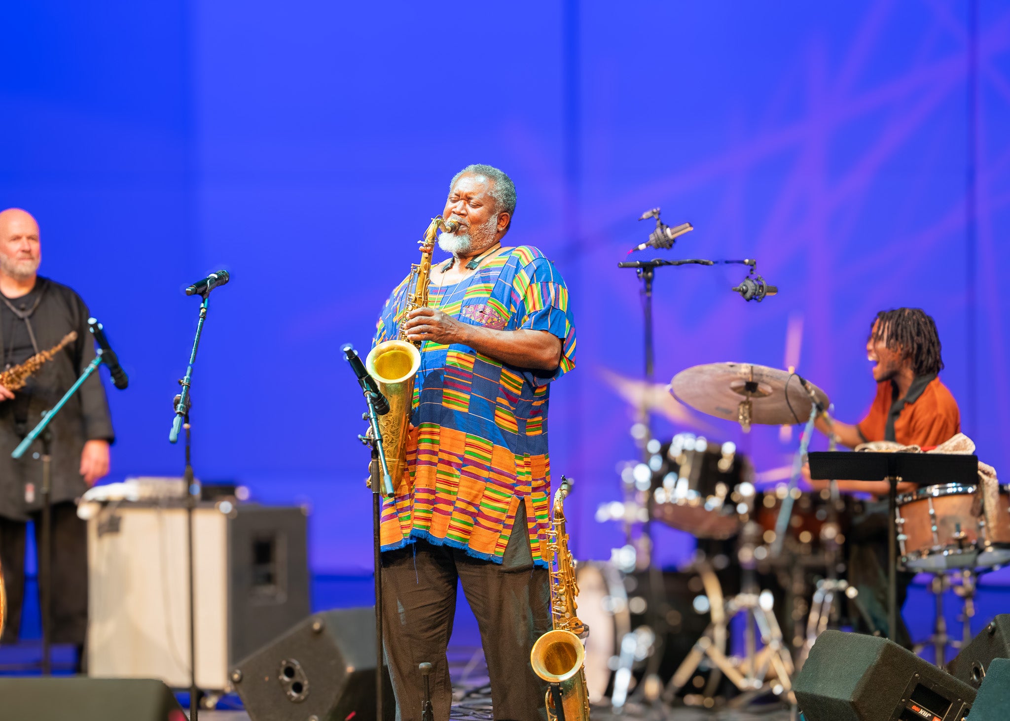 Man wearing a brightly colored blue and gold African tunic playing a saxophone on stage.