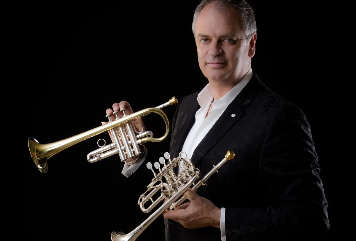 man in black jacket holding two trumpets