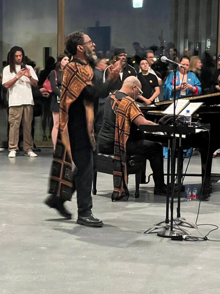 Men performing at an event, one on piano, the other singing and both wearing promotional garb.
