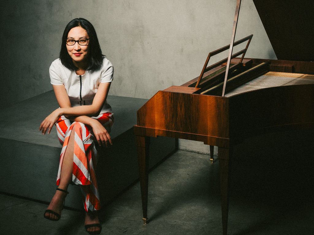 Woman in white shirt, seated, next to a forte piano