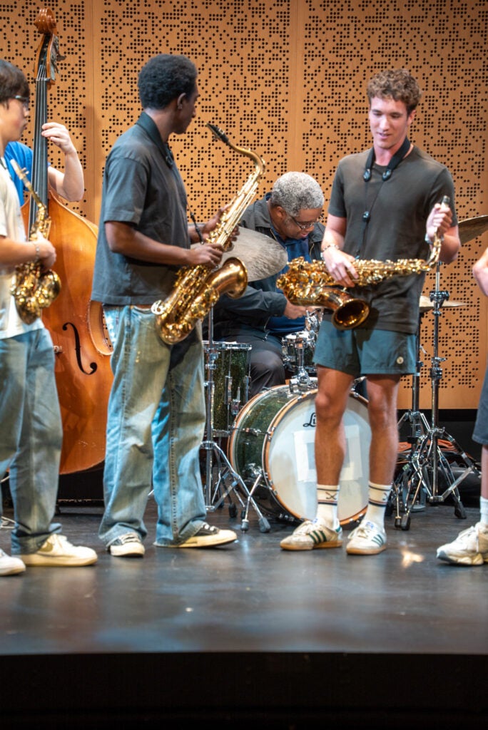 three students on stage with a teacher performing on drums.
