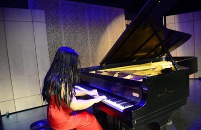 woman in red dress playing a Steinway grand piano.